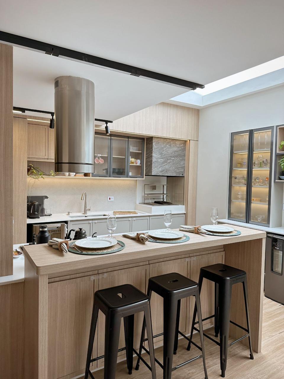 Cozinha planejada contemporânea com ilha em madeira clara e banquetas pretas