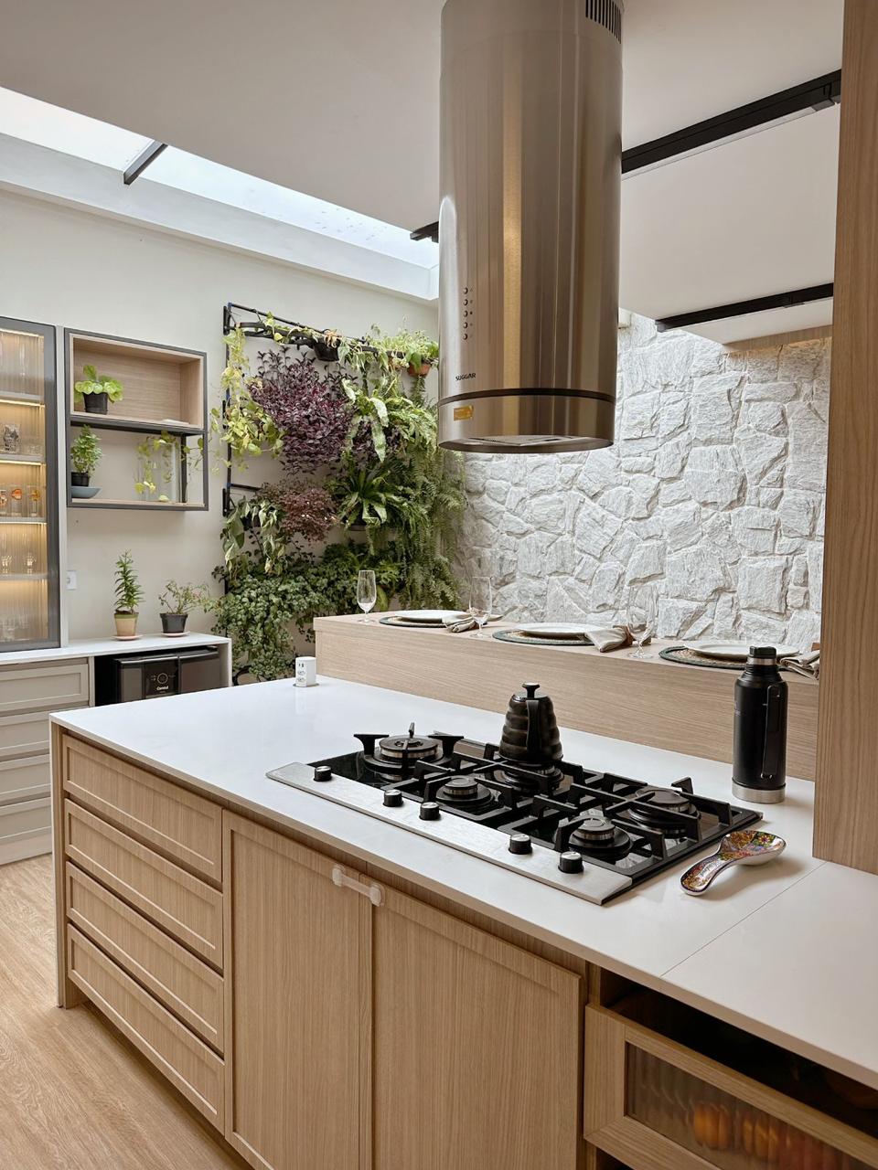 Ilha central com cooktop, coifa cilíndrica e jardim vertical ao fundo