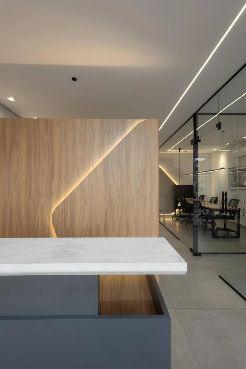 Recepção corporativa com painel de madeira com recortes esculturais e iluminação embutida